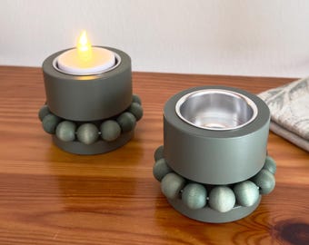 May include: Two teal green candle holders with a ring of wooden beads around the base. Each holder has a small metal cup for a tea light candle.