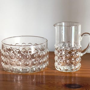 May include: A set of two clear glass bowls with a textured bubble design. The bowl on the left is a sugar bowl and the bowl on the right is a creamer.
