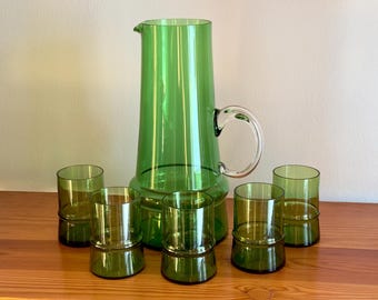 May include: A set of six green glass drinking glasses and a matching pitcher. The glasses have a banded design and the pitcher has a clear handle.