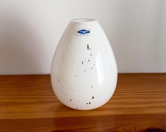 Może przedstawiać: Biały ceramiczny wazon w kształcie łzy z czarnymi plamkami. Wazon ma niebieską etykietę z napisem "Notscheravy Glas".