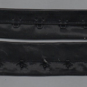 Puede incluir: Extensor de tirantes de sujetador elástico negro con ganchos metálicos. El extensor tiene dos filas de ganchos, cada una con tres ganchos.