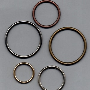 Könnte beinhalten: Fünf Metallringe in verschiedenen Größen und Farben. Die Ringe sind silber, gold und kupferfarben.