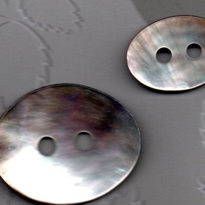 Peut inclure: Deux boutons en nacre irisée avec deux trous chacun. Les boutons sont de forme ovale et ronde.