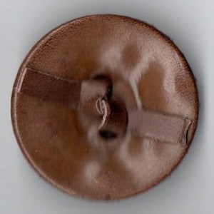 May include: A brown leather button with a stitched design and a hole in the center.