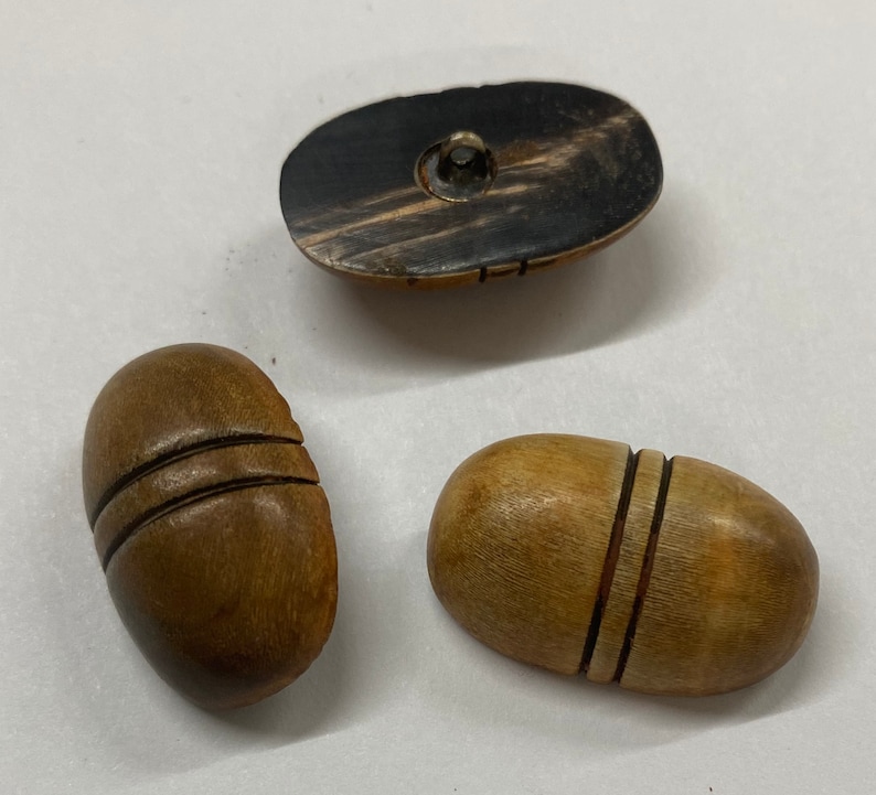K&ouml;nnte beinhalten: Drei Holz-Kn&ouml;pfe, zwei sind hellbraun mit geschnitzten Linien und einer ist dunkelbraun mit einem schwarz-wei&szlig;en Muster.
