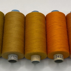 Może przedstawiać: Pięć szpulek nici w odcieniach żółtego, pomarańczowego i brązowego. Szpulki są oznaczone numerami 1472, 2322, 2387, 2412 i 2402.