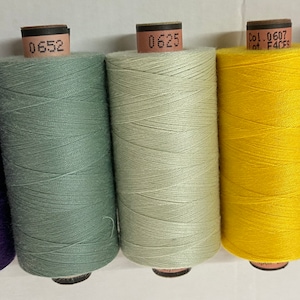 May include: Five spools of thread in different colours: purple, green, light grey, yellow, and red. Each spool has a label with a number on it.