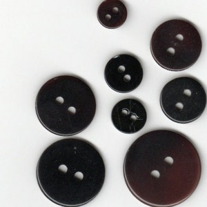 Peut inclure: Assortiment de huit boutons en plastique noir et brun avec deux trous chacun. Les boutons sont de différentes tailles.