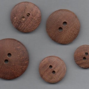 May include: Five brown wooden buttons with two holes each. The buttons are round and have a slightly textured surface.