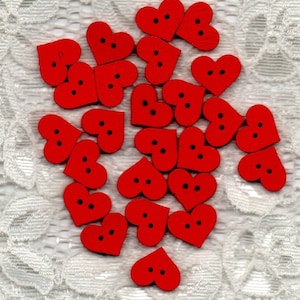 May include: A collection of 20 red wooden heart-shaped buttons with two black holes each. The buttons are scattered on a white lace background.