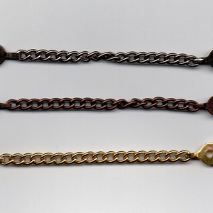 Könnte beinhalten: Drei Metallketten mit ovalen Verschlüssen. Die Ketten sind silber, kupfer und goldfarben.