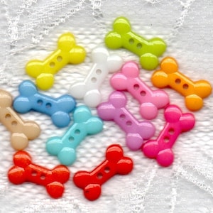 May include: Assortment of colorful plastic bone-shaped buttons. The buttons are in various colors, including yellow, blue, pink, green, orange, red, and white.