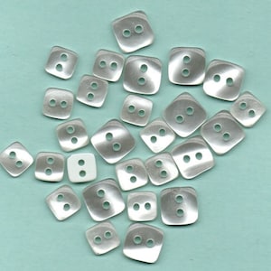 May include: A collection of 25 white, two-hole, square-shaped buttons with rounded edges. The buttons are made of a translucent material, giving them a slightly iridescent appearance.