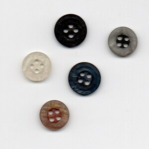 Pode incluir: Cinco botões de diferentes cores com quatro furos cada. Os botões são preto, branco, castanho, cinzento e azul.