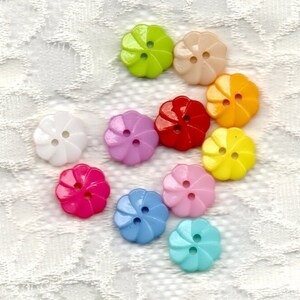 May include: Assortment of 10 colorful plastic flower-shaped buttons with two holes each. The buttons are in shades of pink, red, yellow, green, blue, and white.