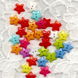 May include: Assortment of colorful star-shaped buttons in various colors, including red, orange, yellow, green, blue, purple, and white. The buttons are arranged in a loose, flowing pattern on a white lace background.