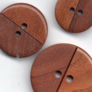 Peut inclure: Trois boutons en bois avec un schéma de couleur brun à deux tons. Chaque bouton a deux trous et est divisé en deux par une ligne droite.