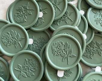 May include: A pile of green wax seals with a floral design. The seals are round and have a raised design of a flower with leaves.