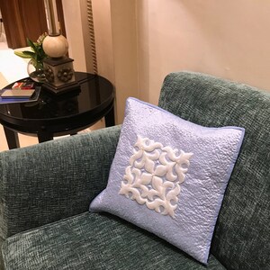 May include: A light blue throw pillow with a white embroidered design on a teal couch.
