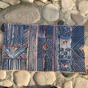 Peut inclure: Un carreau de céramique bleu et rouge avec un motif géométrique. Le carreau est fait de petites pièces de céramique texturées.