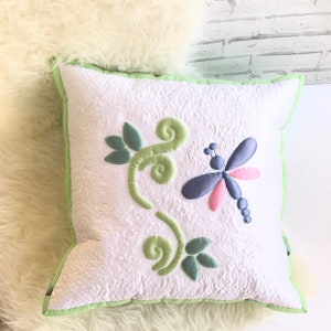 Peut inclure: Oreiller blanc avec une bordure verte et une libellule brodée verte, bleue et rose ainsi que des feuilles.