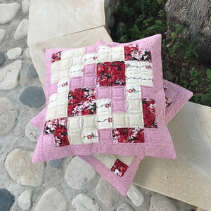 Puede incluir: Dos almohadas de tiro con estampado floral rosa y crema con un diseño acolchado. Las almohadas están sobre una superficie de piedra.