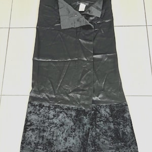 May include: A black skirt with a satin finish and a velvet hem. The skirt has a button closure at the waist and a split front design. The skirt is a midi length.