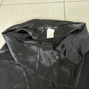 May include: Black satin top with a unique asymmetrical collar and a single button closure. The top has a smooth, shiny texture and a relaxed fit. The tag reads "YOHJI YAMAMOTO NOR".