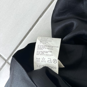 May include: A close-up of a black garment with a care label attached. The label provides instructions for cleaning, including dry cleaning with perchloroethylene and warm ironing with a press cloth. The label also includes the text "NE-S04-900."