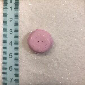 May include: A pink button with a textured surface and two holes in the centre. The button is approximately 2.5 cm in diameter.