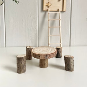 Könnte beinhalten: Ein Miniatur-Feengarten-Set mit einer Holztür und Leiter, einem kleinen runden Tisch und vier Baumstammhockern. Die Tür hat dekorative Akzente, und der Tisch und die Hocker sind aus Naturholz.
