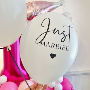 Peut inclure: Ballon blanc avec le texte "Just Married" en &eacute;criture noire avec un petit c&oelig;ur noir sous le texte. Le ballon est attach&eacute; avec un ruban blanc et est entour&eacute; de ballons roses et blancs.