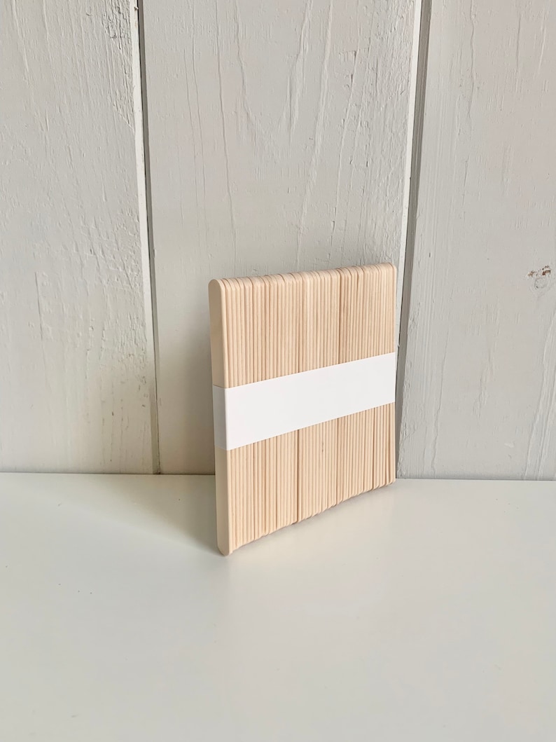 May include: A bundle of natural wooden craft sticks, approximately 100 sticks, arranged in a square shape. The sticks are bundled together with a white paper band.