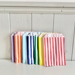 May include: A set of ten striped paper bags in various colors, including purple, orange, light blue, navy blue, green, yellow, and red. The bags are all folded and stacked together.