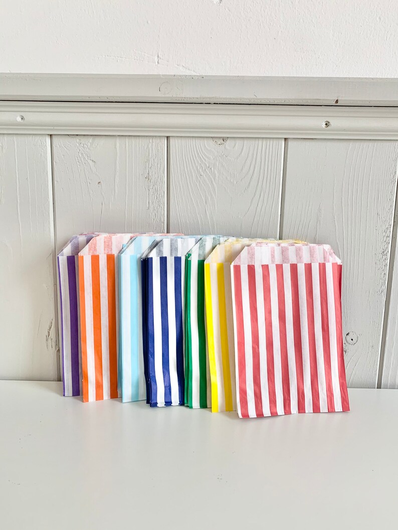 May include: A set of ten striped paper bags in various colors, including purple, orange, light blue, navy blue, green, yellow, and red. The bags are all folded and stacked together.