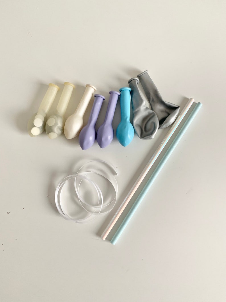 May include: A set of party supplies including balloons, straws, and ribbon. The balloons are in shades of blue, white, and gray. The straws are white and blue. The ribbon is white.