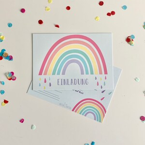 May include: A rainbow-themed invitation card with the text "EINLADUNG" and "auf Dich!" printed on it. The card features a colorful rainbow with raindrops and a white background.