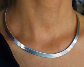 Può includere: Una collana a catena d'argento con un design piatto e largo. La collana è realizzata in metallo liscio e lucido e ha uno stile semplice ed elegante.
