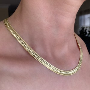 Puede incluir: Un collar de cadena de oro con un diseño texturizado en forma de serpiente.