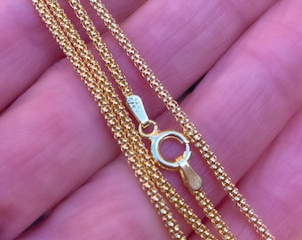 Puede incluir: Un collar de cadena de oro con un pequeño cierre redondo. La cadena está hecha de pequeñas cuentas enlazadas.