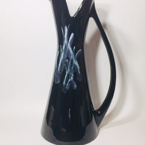 May include: A black ceramic pitcher with a unique, curved design and a stylized blue and green floral pattern.