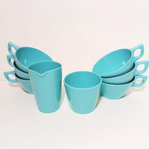 May include: Set of six turquoise blue plastic cups and a matching pitcher. The cups are stacked in pairs and the pitcher is in front of the cups.