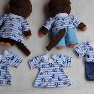 Könnte beinhalten: Zwei Affenpuppen in blau-weiß gestreiften Matrosenoutfits mit maritimen Mustern. Dazu passende Outfits und blaue Jeansshorts. Mehrere passende Kleidungsstücke sind ebenfalls abgebildet.