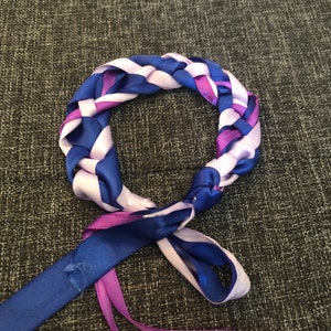May include: A braided headband made from purple, blue, and white satin ribbon. The headband is tied in a knot at the back.