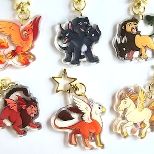 May include: Six colourful acrylic charms featuring mythical creatures. The charms are attached to gold keychains with star-shaped rings. The creatures include a phoenix, a three-headed dog, a chimera, a griffin, a pegasus, and a manticore.