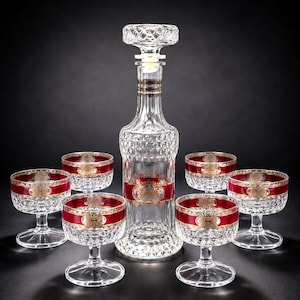 May include: A crystal decanter set with a diamond pattern, featuring a decanter and six glasses. The set has red and gold accents. The glasses have a short stem and a wide bowl. The decanter has a stopper.