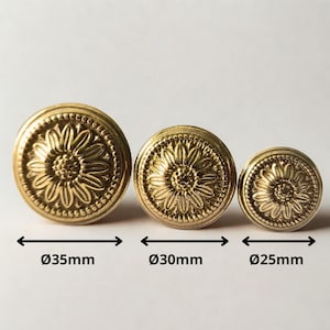 Peut inclure: Trois boutons de meuble en laiton antique avec un motif de tournesol. Le plus grand bouton mesure 35 mm de diamètre, le milieu 30 mm et le plus petit 25 mm. Chaque bouton présente un motif floral détaillé et un bord perlé.