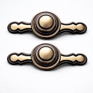 Può includere: Due maniglie per mobili in stile antico con centro circolare e maniglie decorative. Le maniglie sono in metallo color bronzo con bordo marrone scuro, perfette per aggiungere un tocco vintage ai mobili.
