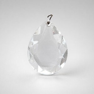Op de afbeelding: Een heldere, facetgeslepen kristallen druppelhanger met een kleine metalen lus aan de bovenkant. Het kristal is transparant, reflecteert licht en toont zijn geometrische sneden. Ideaal voor kroonluchters of decoratieve accenten.