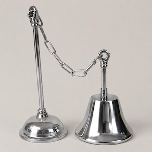 May include: Two polished chrome-plated bell-shaped objects linked by a chain. One is a tall, slender post with a rounded base. The other is a bell-shaped object with a flared base. The chain is made of small, interlocking links.